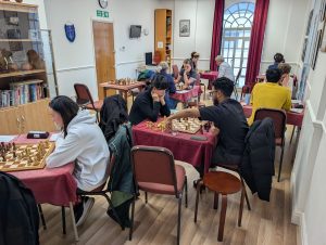 A busy room of adults playing chess with clocks and wooden chess sets at Hammersmith Chess Club